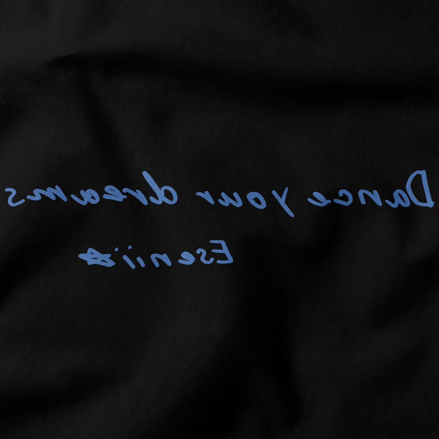 Close-up of Dance Your Dreams T-Shirt by Eseniia, showcasing the backward text design in black